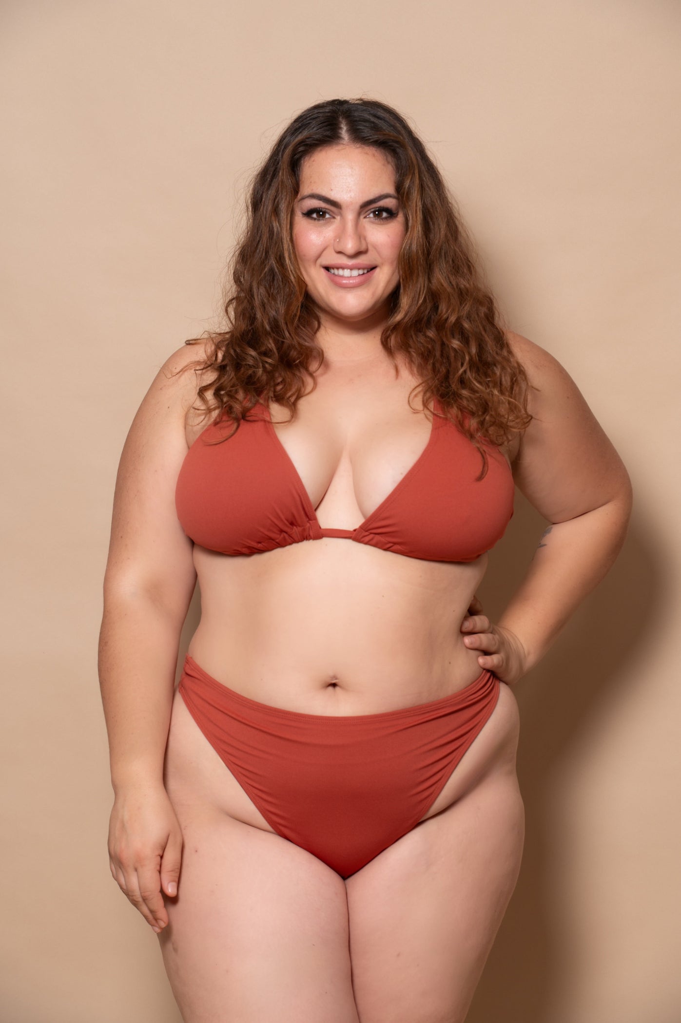 plussize woman wearing a rust red bikini set against a beige background