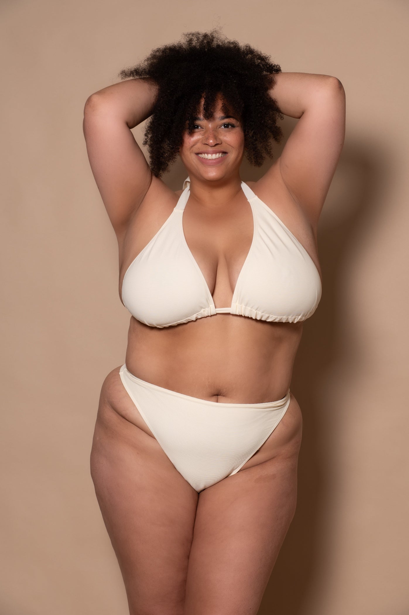 plussize woman wearing a white cream bikini against a beige background