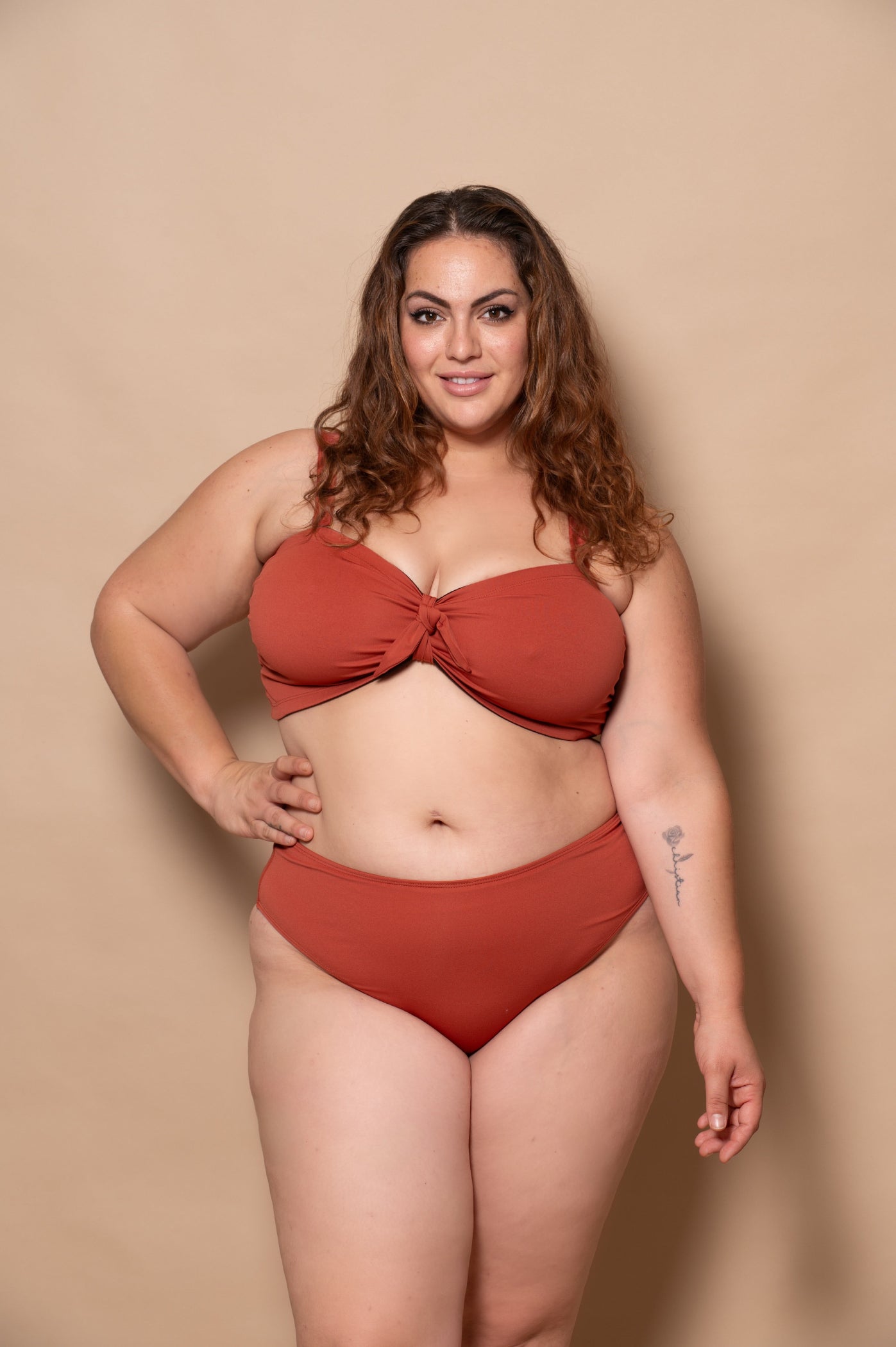 plussize woman wearing a rust red bikini set against a beige background
