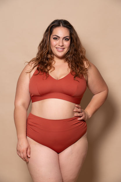 curvy woman wearing a rust red bikini set against a beige background