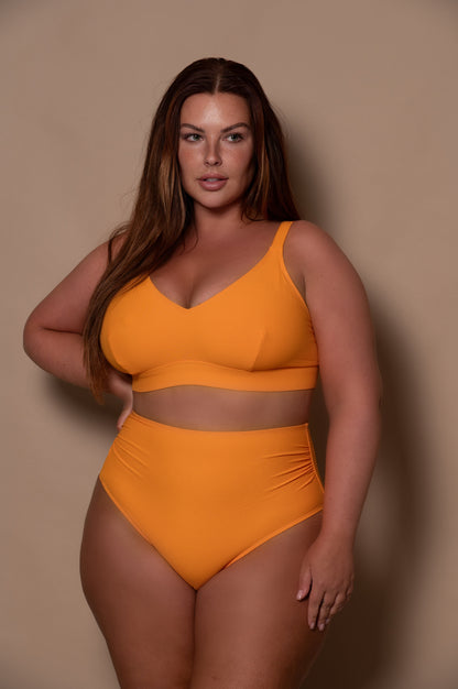 curvy woman wearing a yellow bikini against a beige background