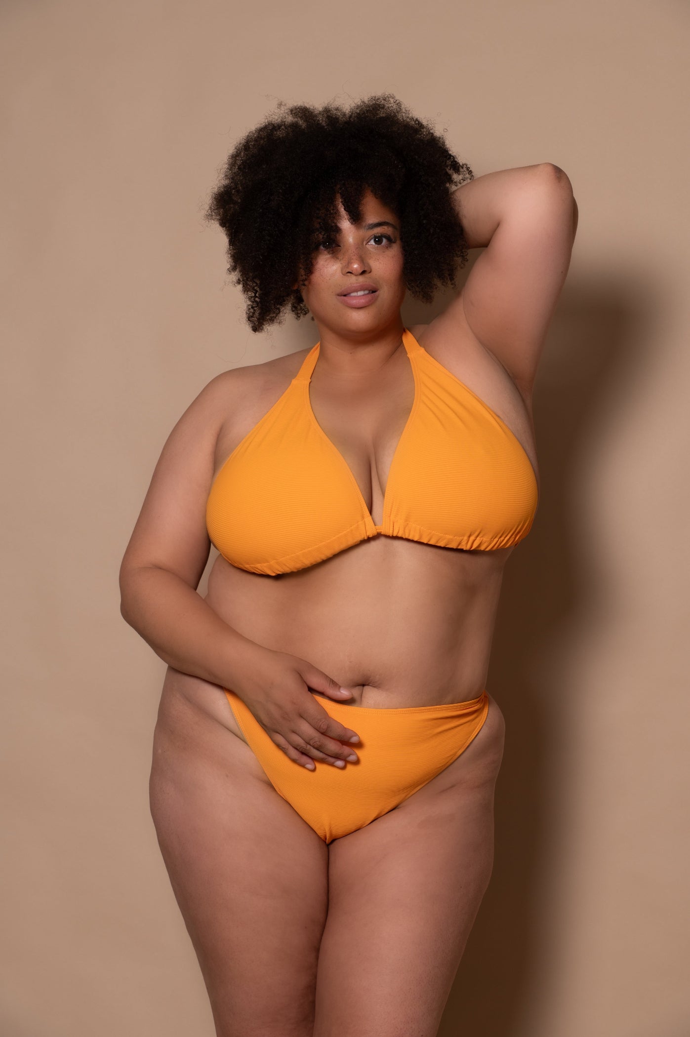 plussize woman wearing a yellow bikini against a beige background