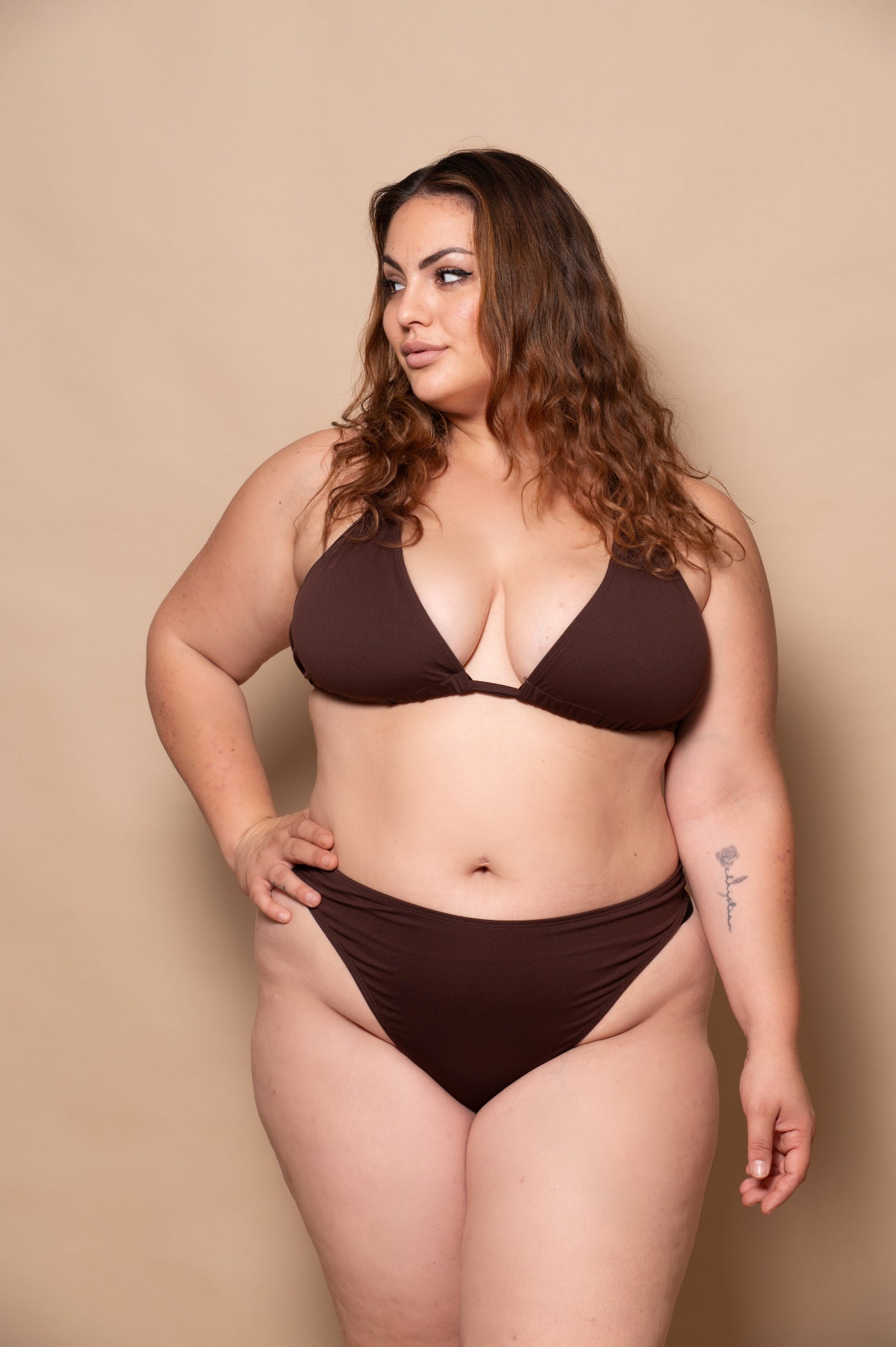 plussize woman wearing a chocolate brown bikini  against a beige background