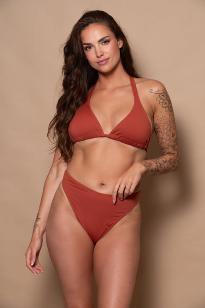 woman wearing a rust red bikini  against a beige background