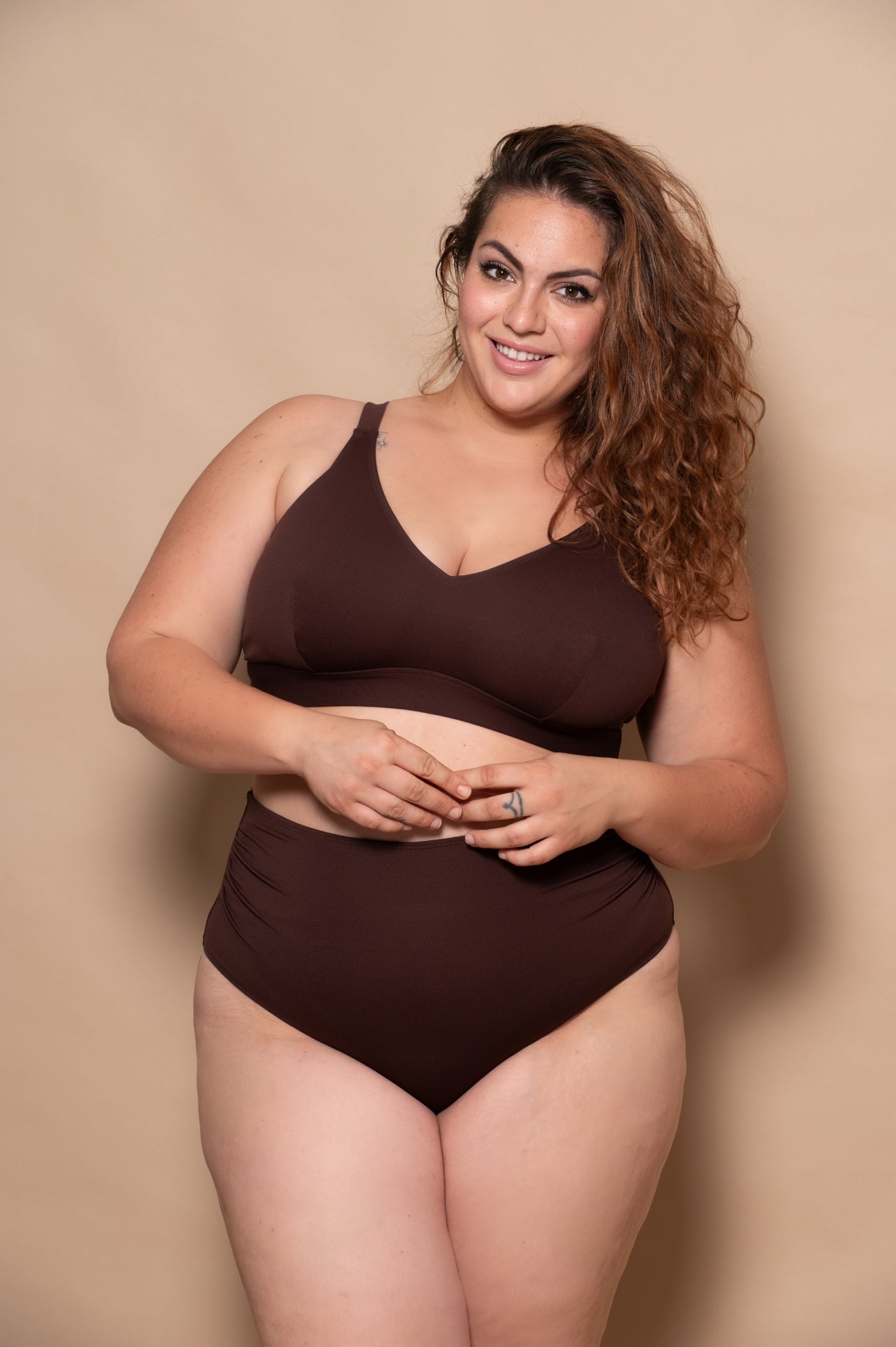 plussize woman wearing a chocolate brown bikini  against a beige background