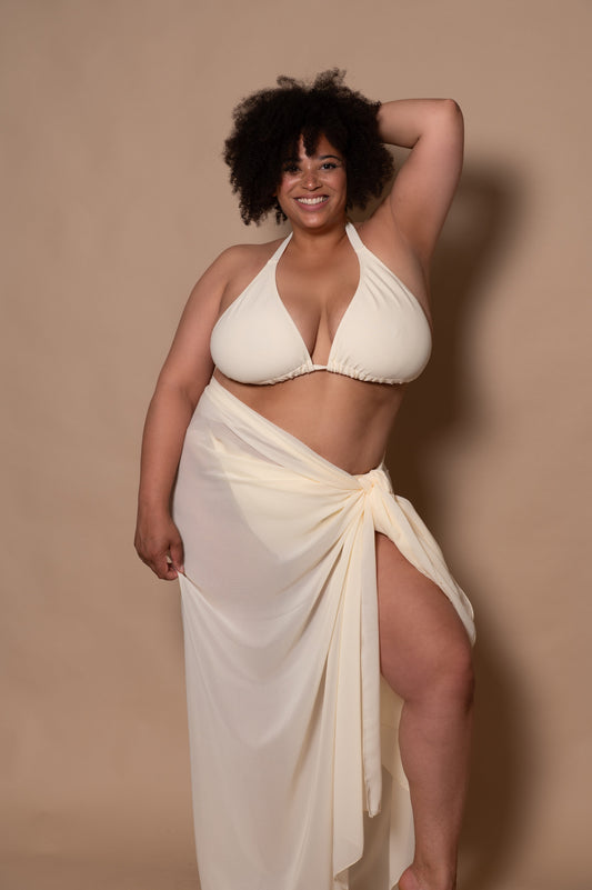 plussize woman wearing a white cream bikini with pareo cover up against a beige background