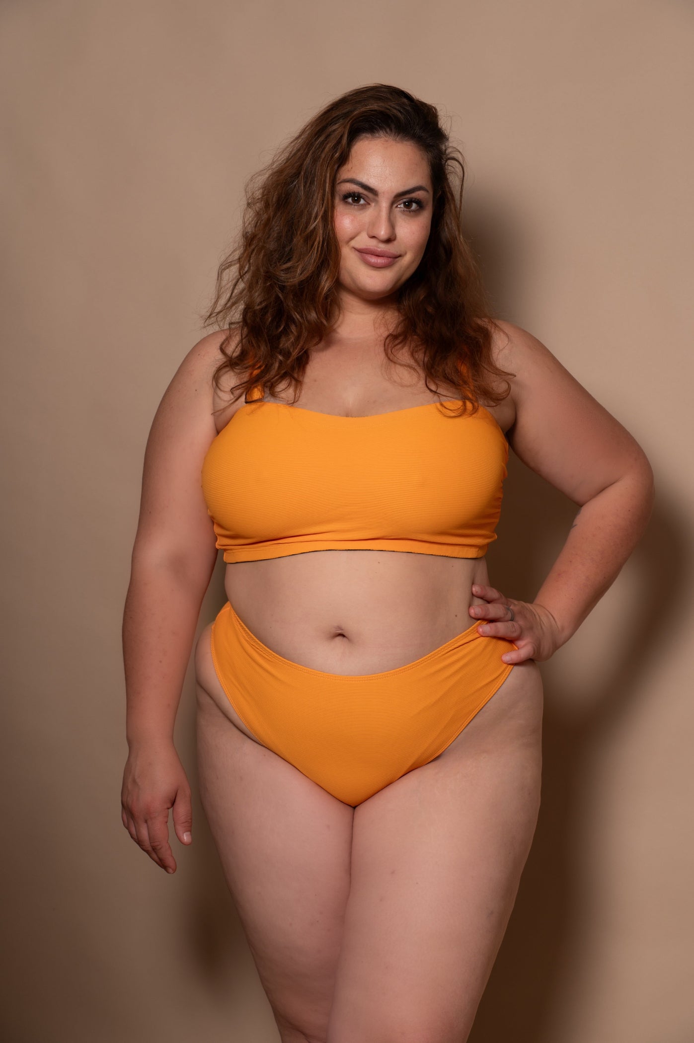 plussize woman wearing a yellow sunflower bikini against a beige background
