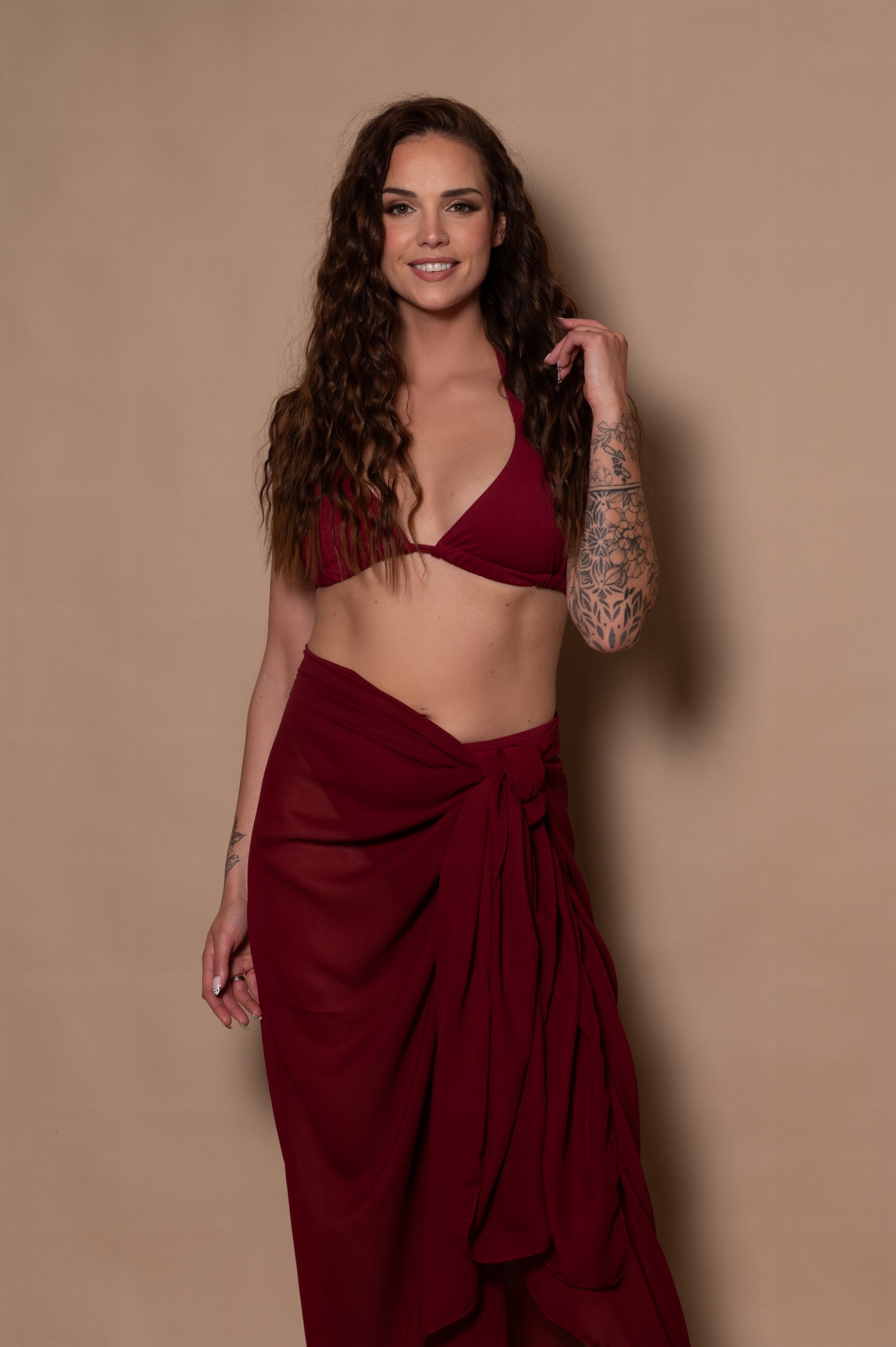 Woman wearing a burgundy bikini and skirt against a beige background
