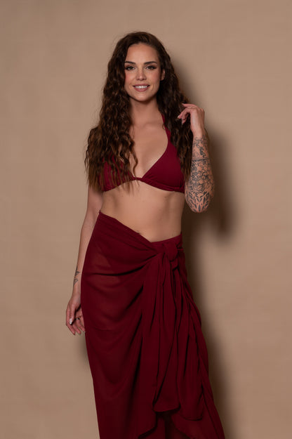 Woman wearing a burgundy bikini and skirt against a beige background