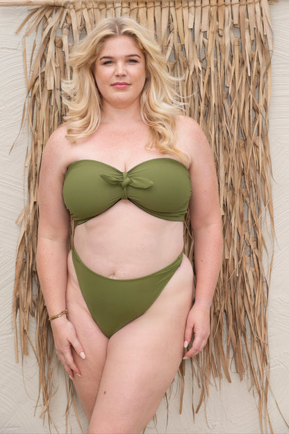 Woman wearing a green bikini standing in front of a thatched wall.