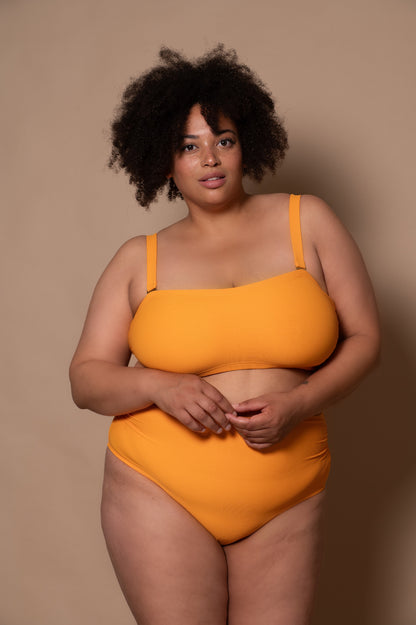 plussize woman wearing a yellow sunflower bikini against a beige background