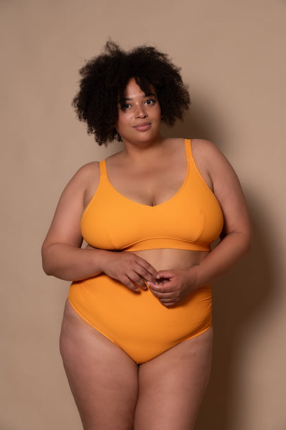 plussize woman wearing a yellow bikini against a beige background