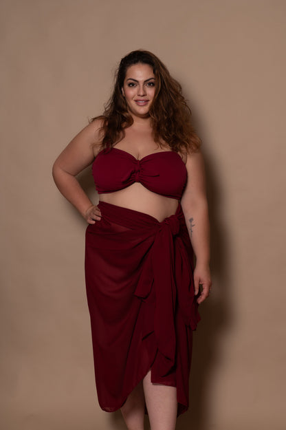 plussize woman wearing a wine red bikini  and pareo cover up against a beige background