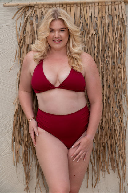 curvy woman wearing a red bikini set standing against a textured wall with decorative elements.