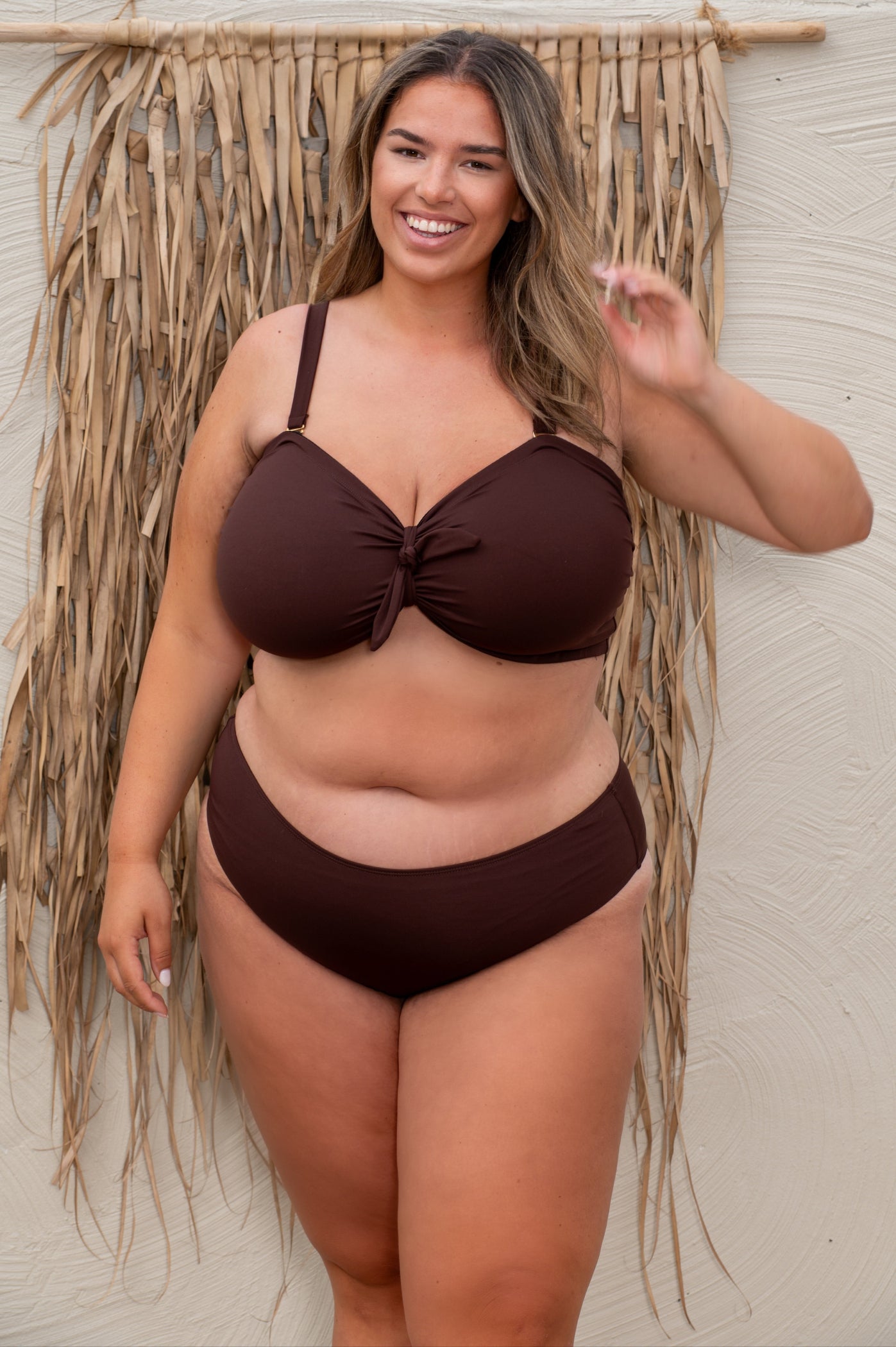 plussize woman wearing a chocolate brown bikini  against a beige background