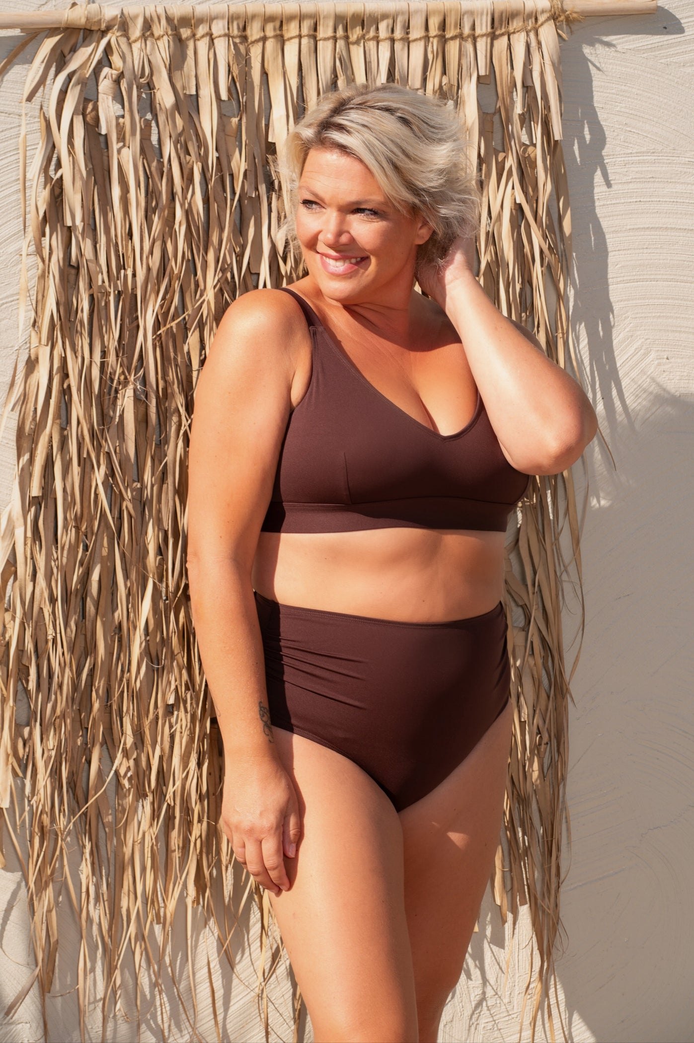 Woman wearing a brown bikini standing against a textured wall.