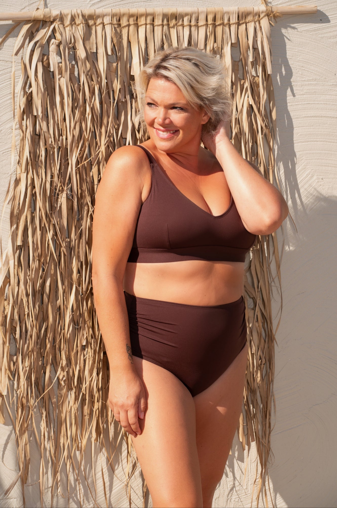 Woman wearing a brown bikini standing against a textured wall.