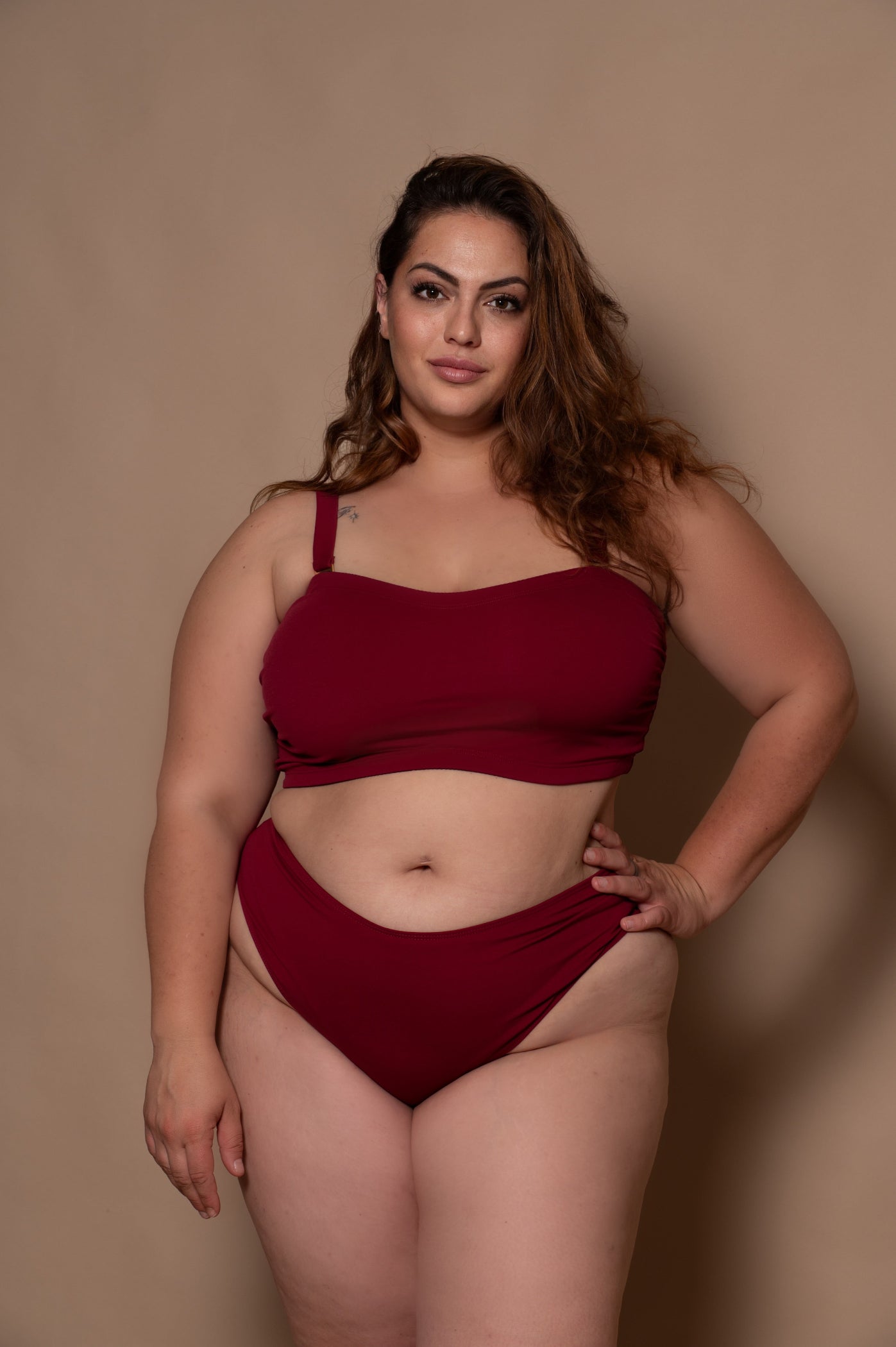 plussize woman wearing a wine red bikini against a beige background