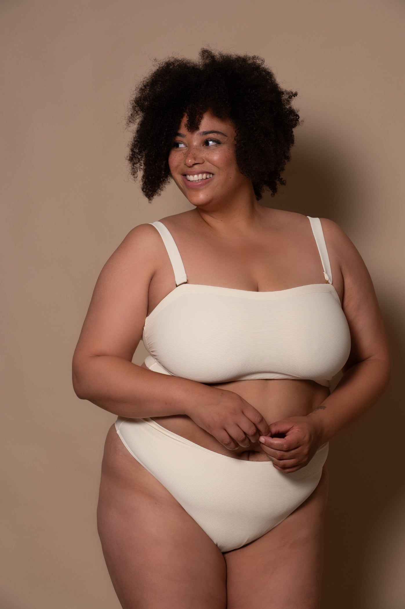 plussize woman wearing a white cream bikini against a beige background
