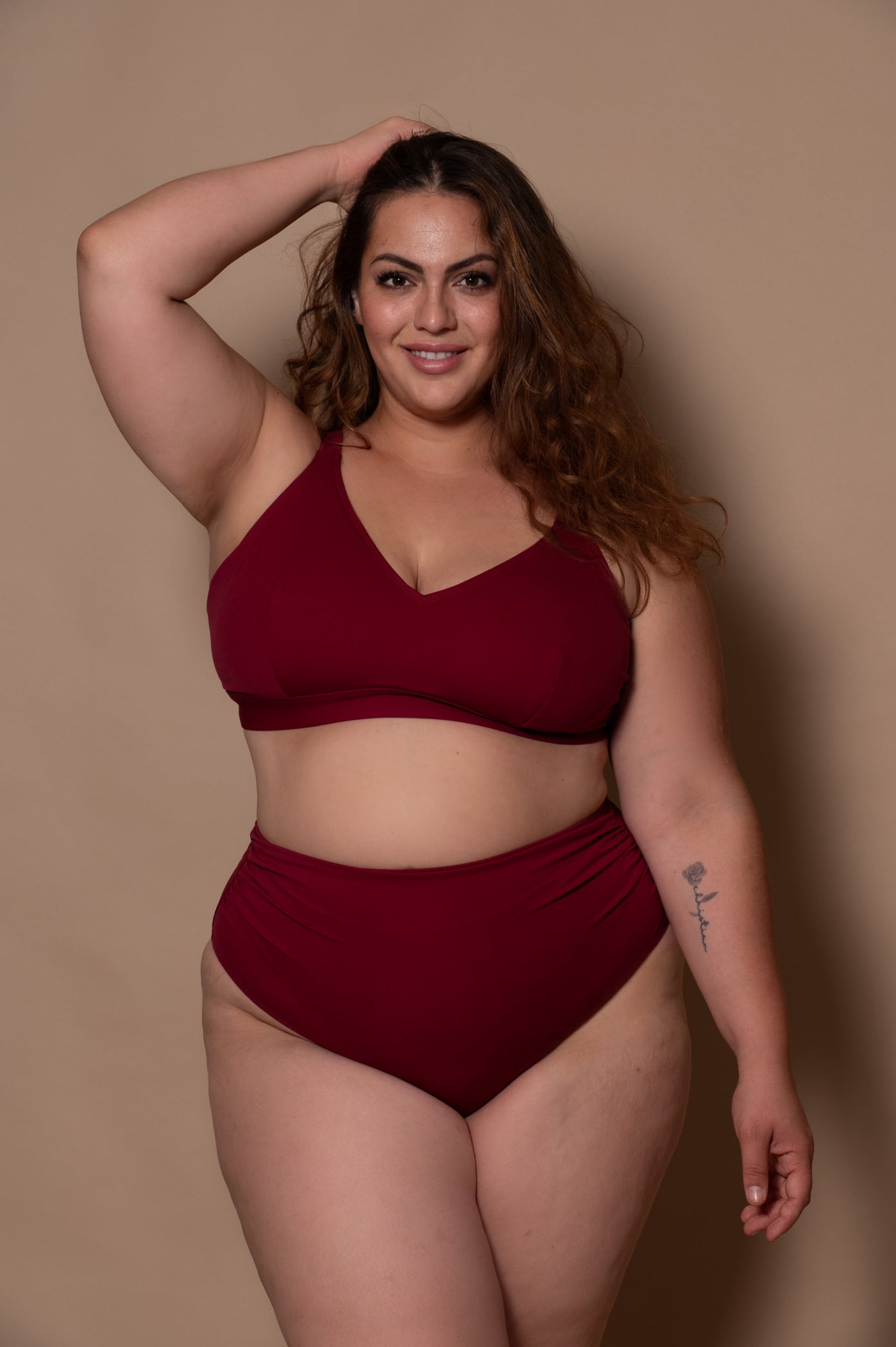 plussize woman wearing a wine red bikini against a beige background