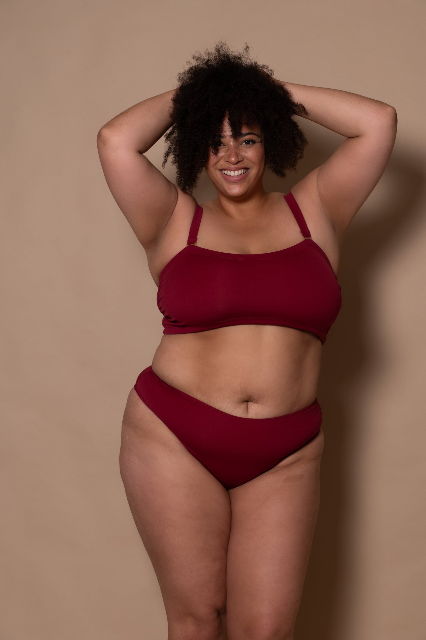 plussize woman wearing a wine red bikini against a beige background