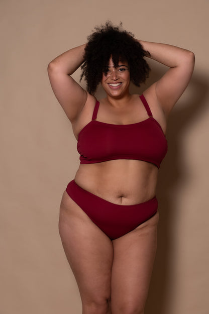 plussize woman wearing a wine red bikini against a beige background