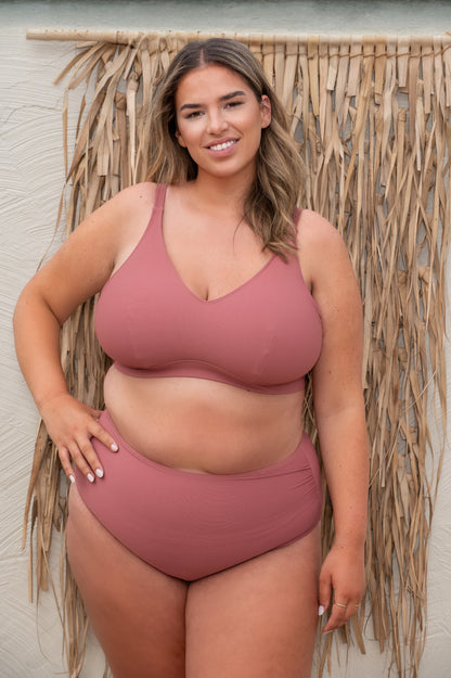 plussize woman wearing a pink - rosewood bikini standing against a textured wall.