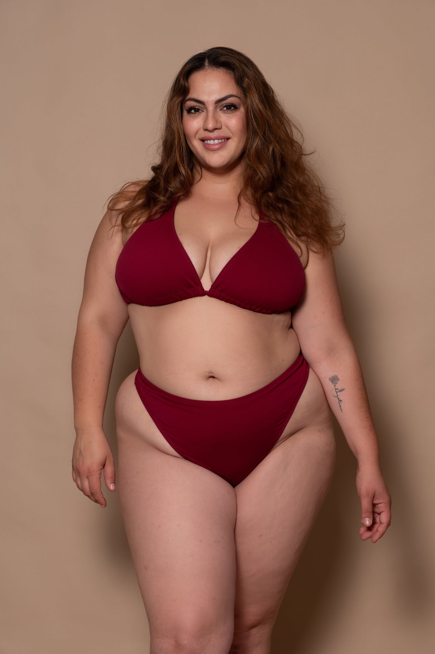 plussize woman wearing a wine red bikini  against a beige background