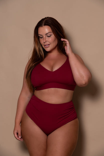curvy woman wearing a wine red bikini against a beige background