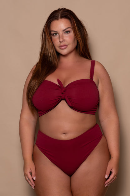 plussize woman wearing a wine red bikini against a beige background