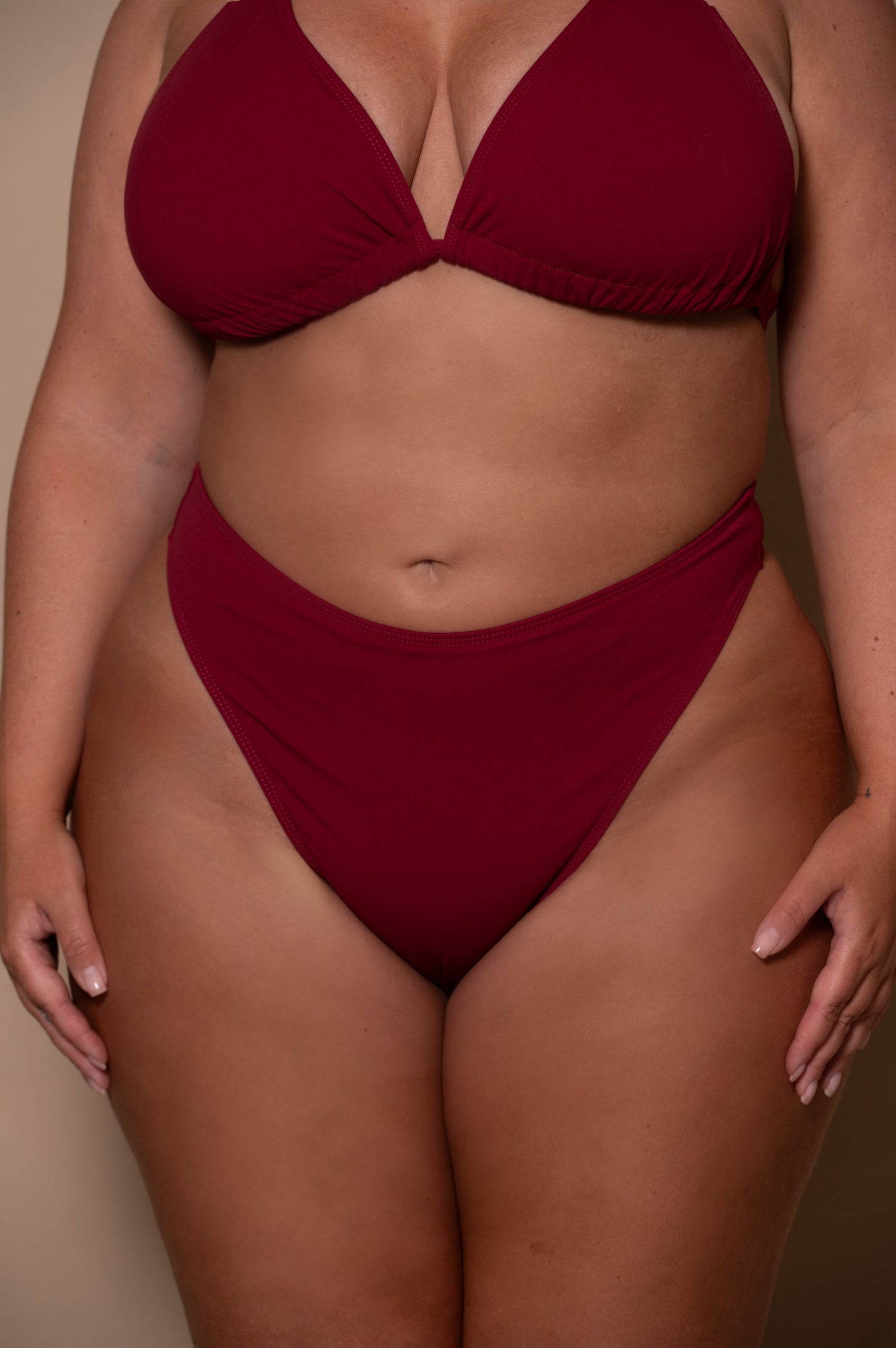 plussize woman wearing a wine red bikini  against a beige background