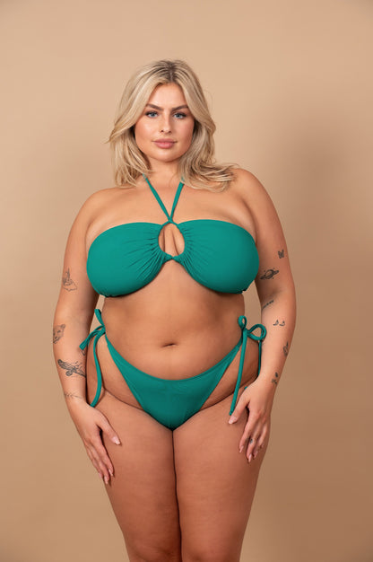 Curvy woman wearing an emerald green bikini against a beige background