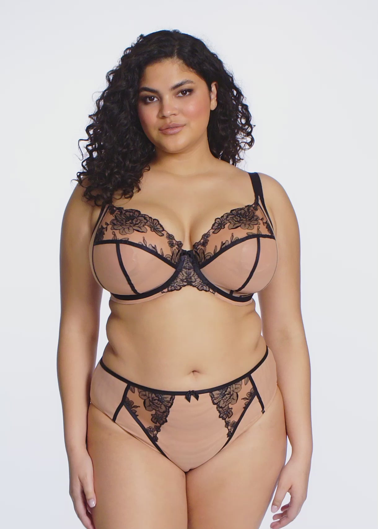 curvyoman wearing a beige lingerie set with black straps and black lace on a white background
